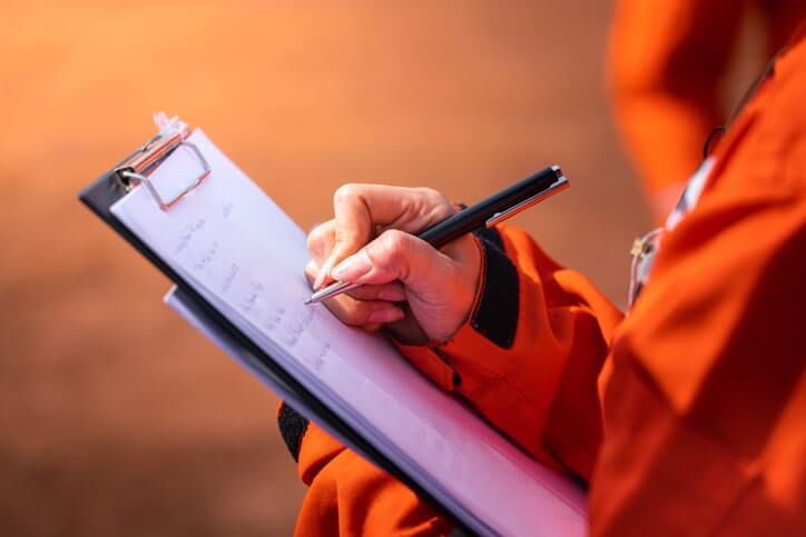 Worker writing on an EHS audit clipboard with a pen